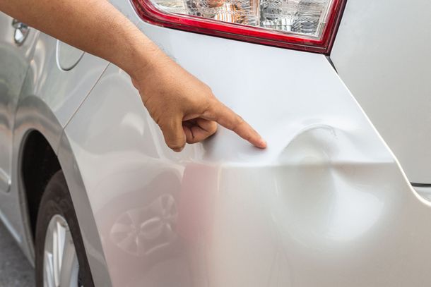 Hand pointing to a dent on the rear side of a white car