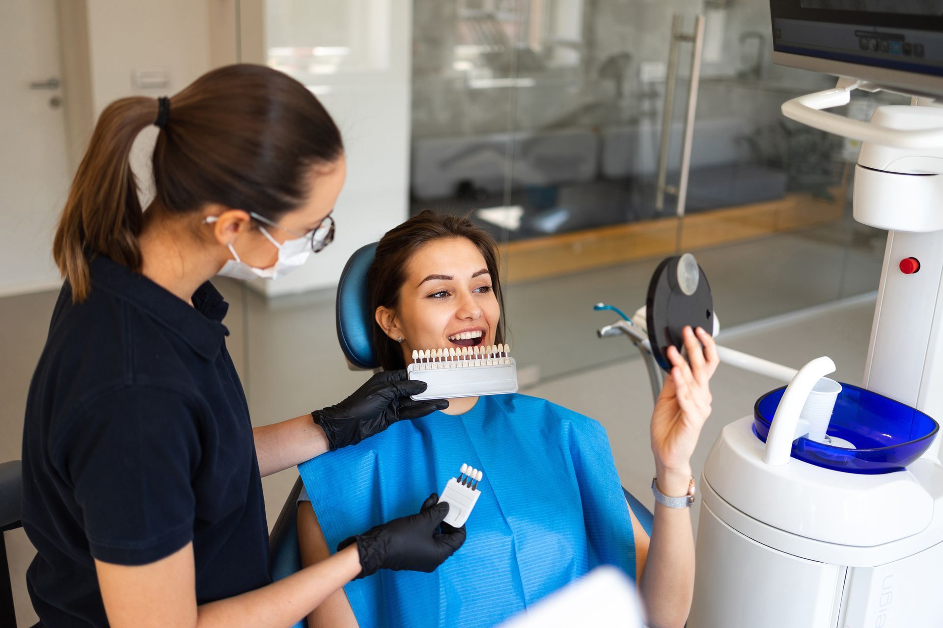 Dentist matching patient's teeth to a shade guide in a dental office.