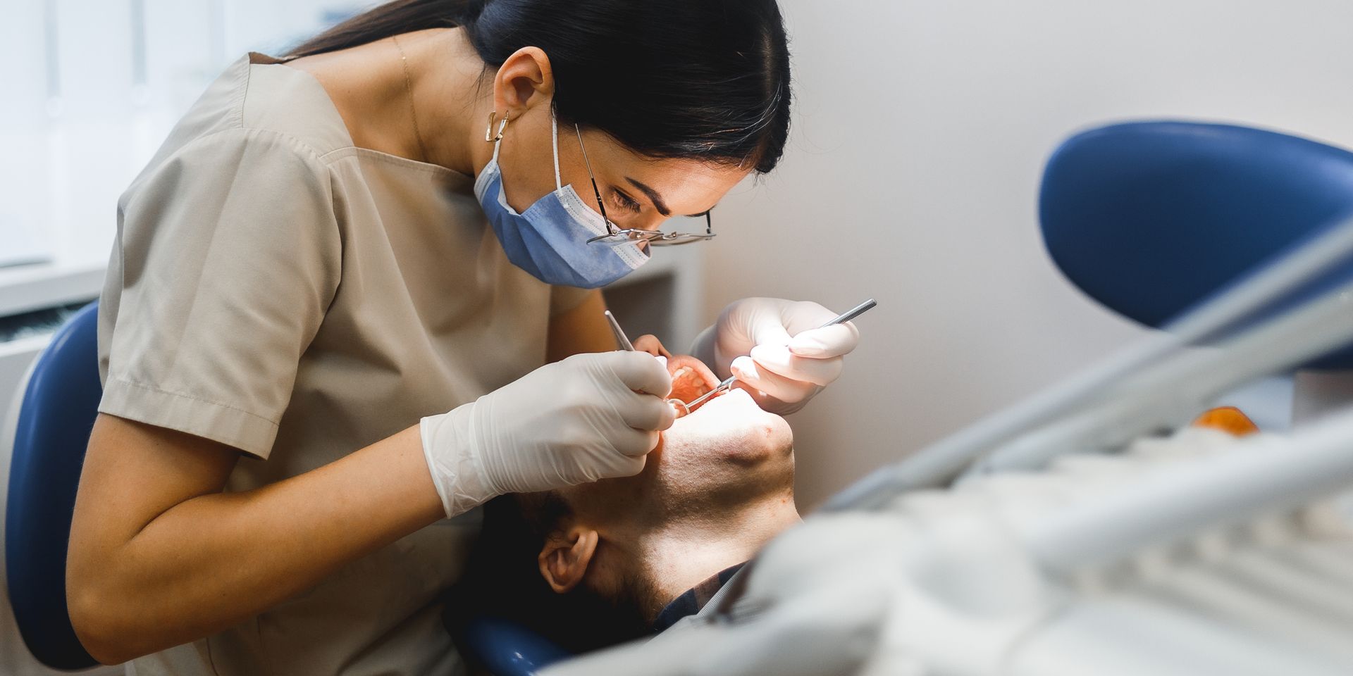 Dentist in mask examining patient's teeth in dental office.