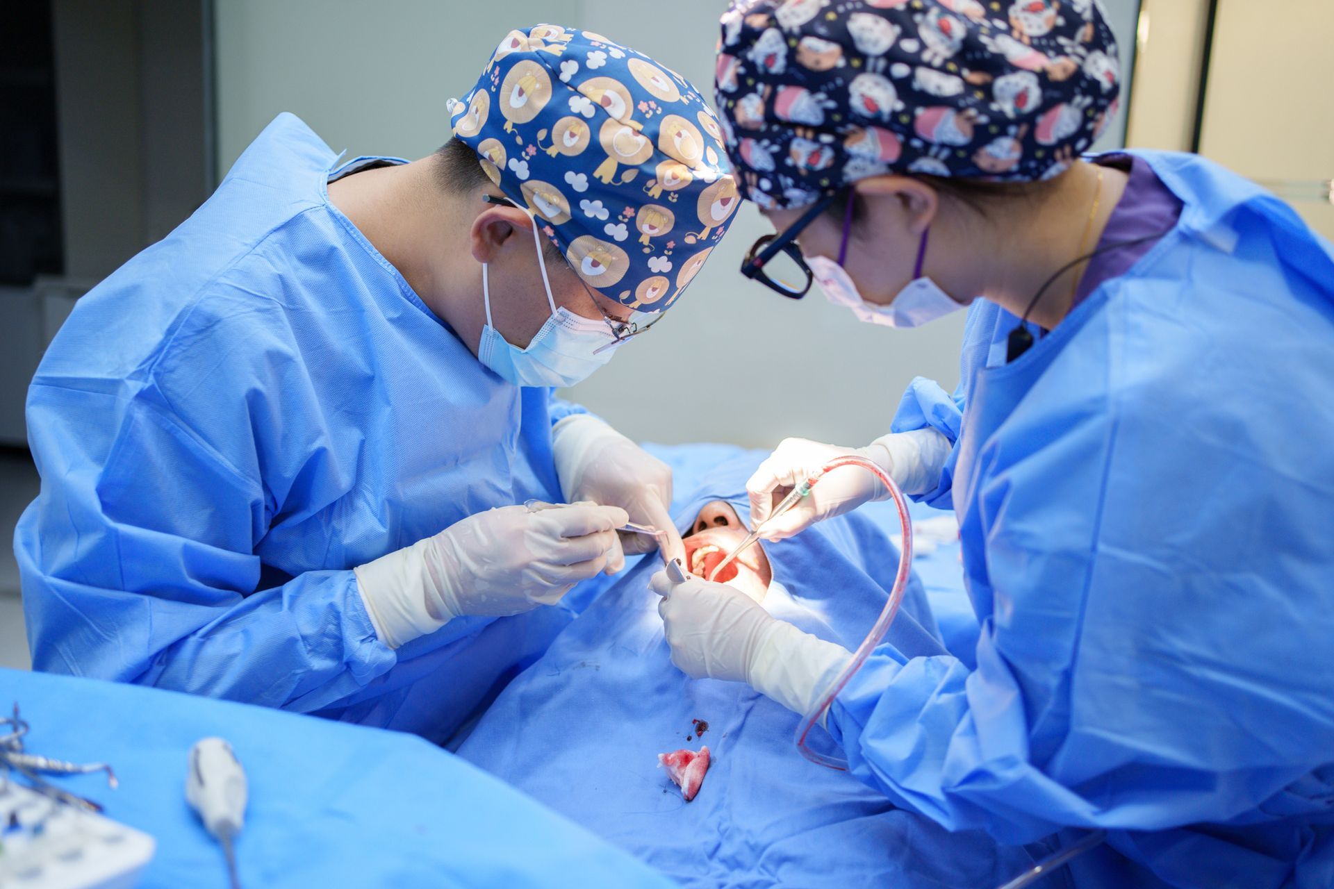 Two surgeons in blue scrubs perform surgery on a patient's face in an operating room.