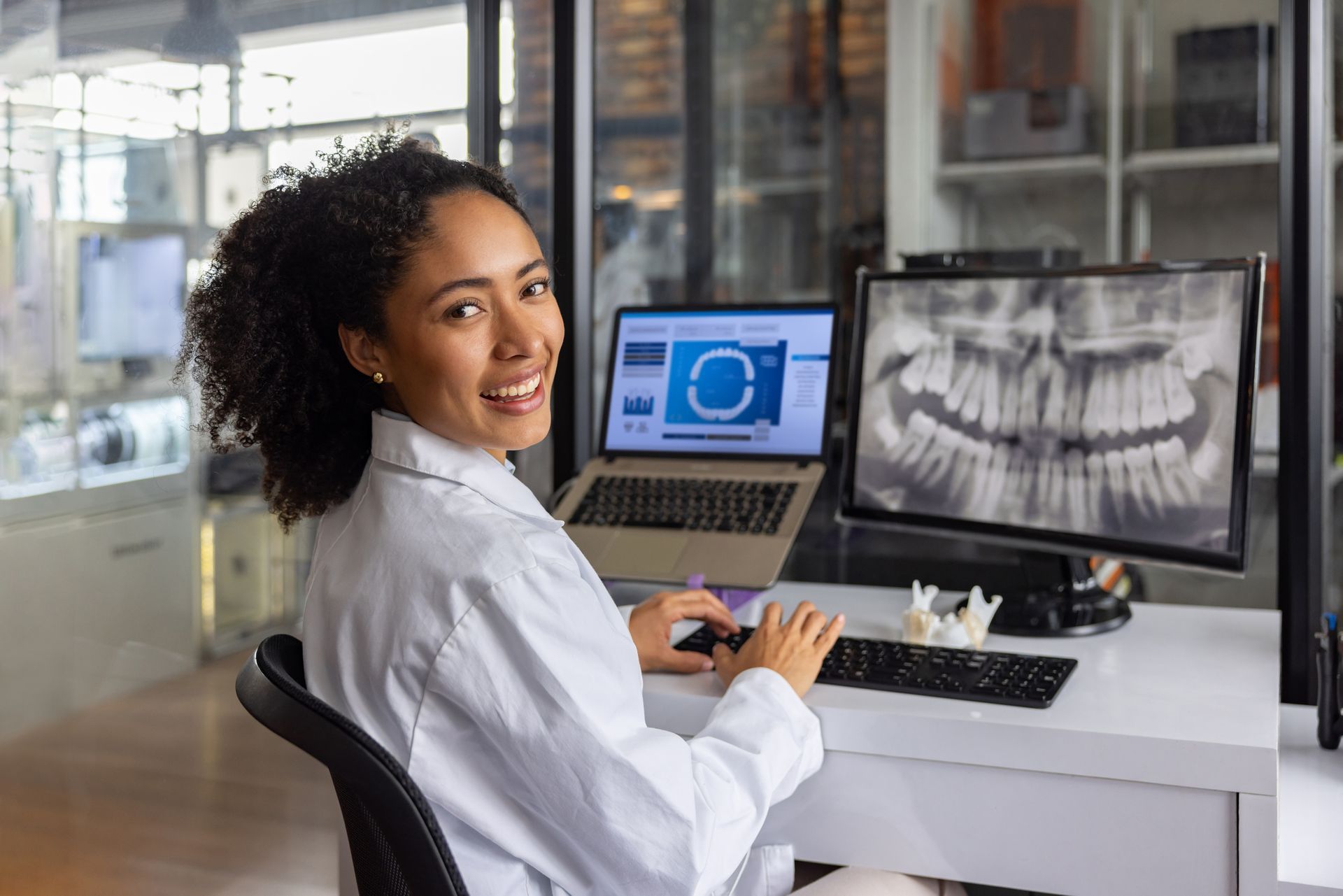Smiling dentist reviewing dental x-rays on a computer. In a clinic setting.