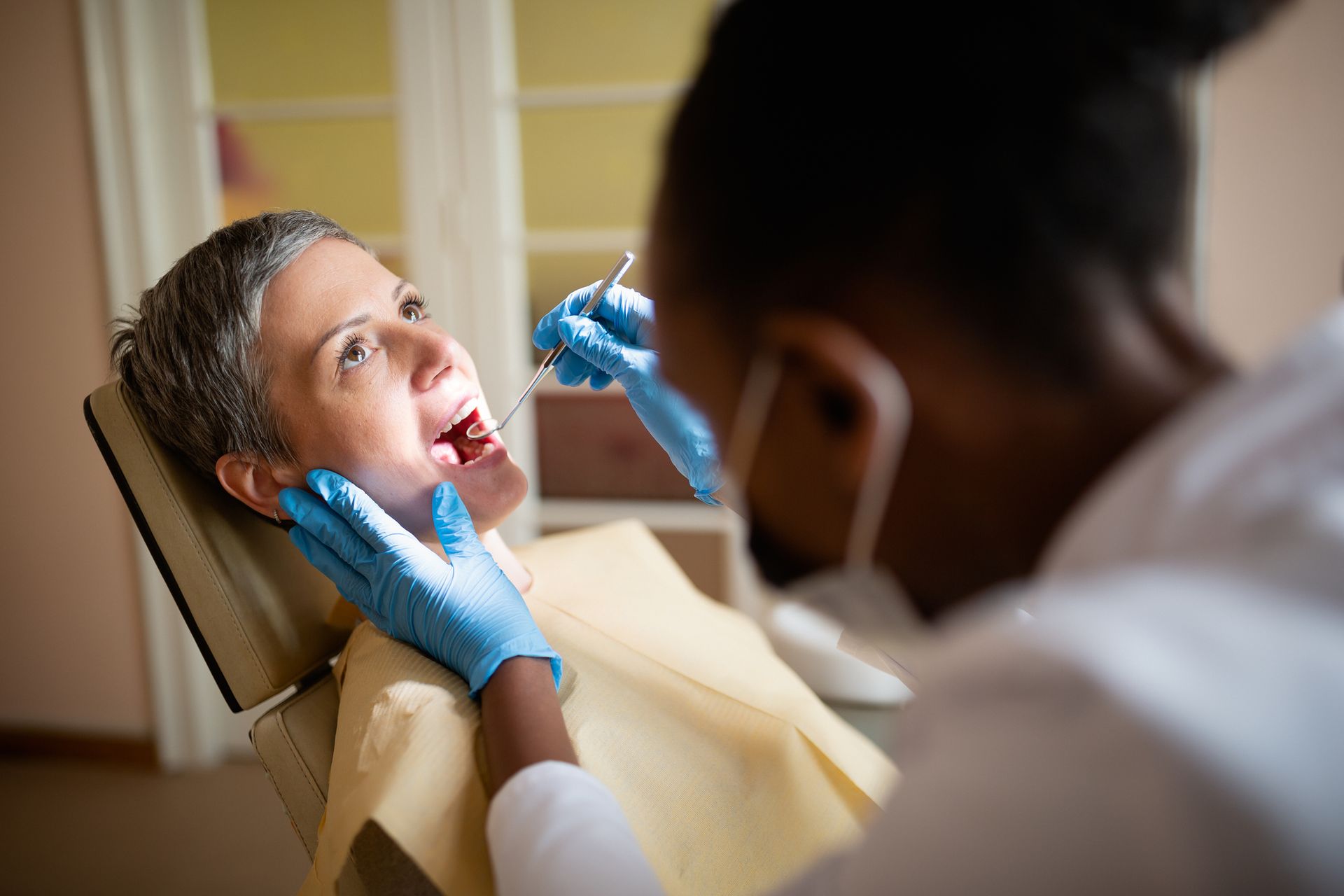A dentist examining a patient's teeth with tools. Patient is in a chair, mouth open.