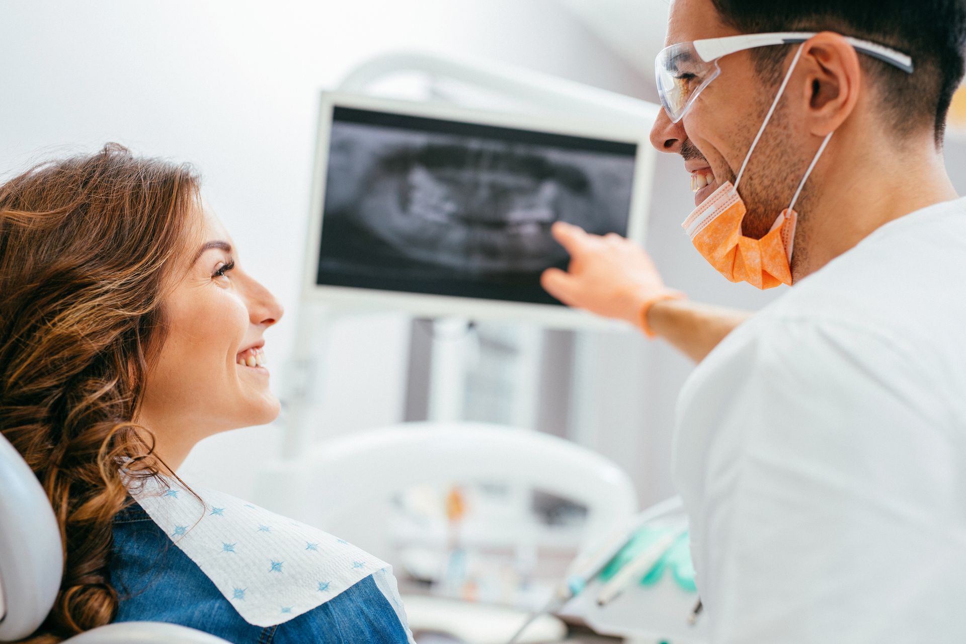 Dentist pointing at dental X-ray, smiling at patient in a dental office.