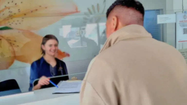 Woman at dentist, smiling, comparing tooth shade to a chart. Dentist holds a mirror.