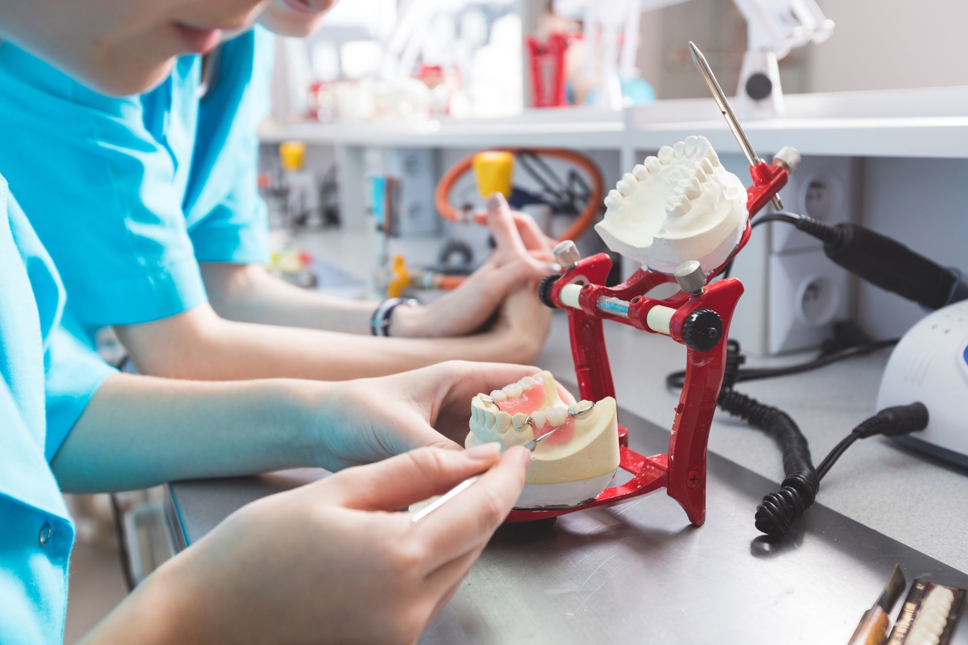 Two people working on dental models in a lab; one holding a model, another working with a tool.
