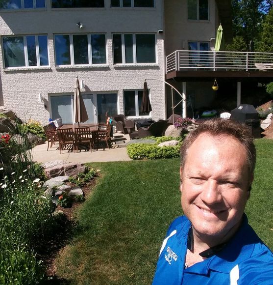 A man in a blue shirt is standing in front of a house. Devine Shine Window Cleaning Canton MI.
