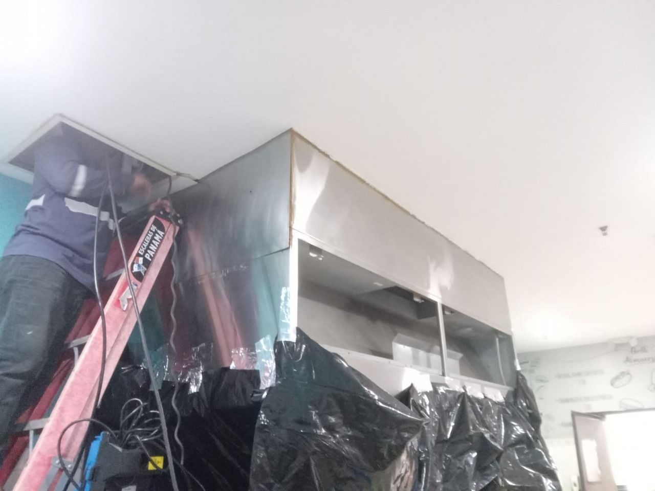 Un hombre en una escalera trabajando en una pared de acero inoxidable.