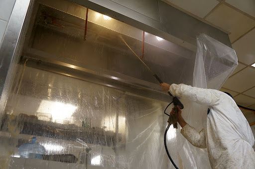 Un hombre está limpiando una campana de cocina con una lavadora de alta presión.
