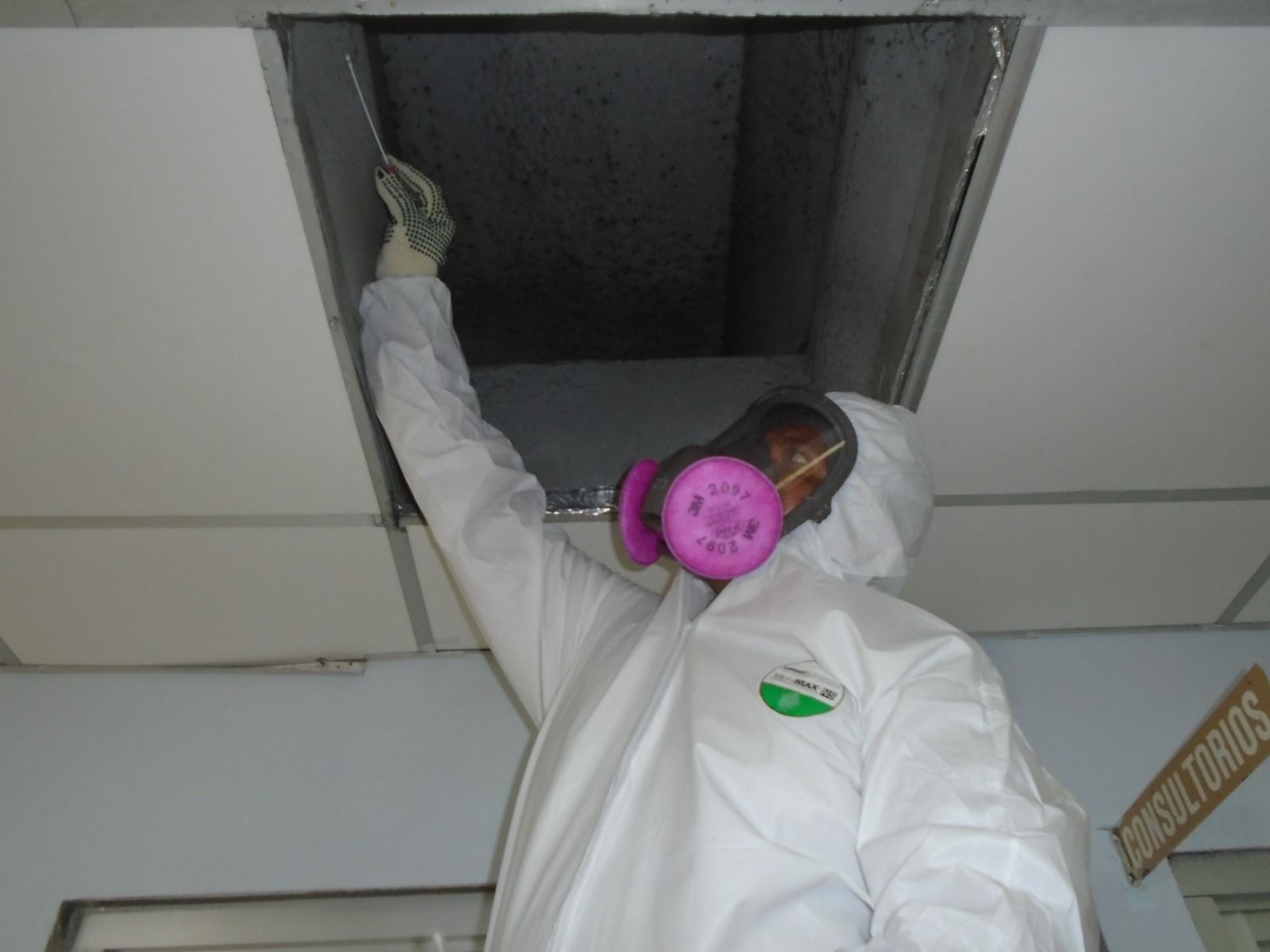 Una persona que lleva un traje de protección y una máscara mira a través de un agujero en el techo.