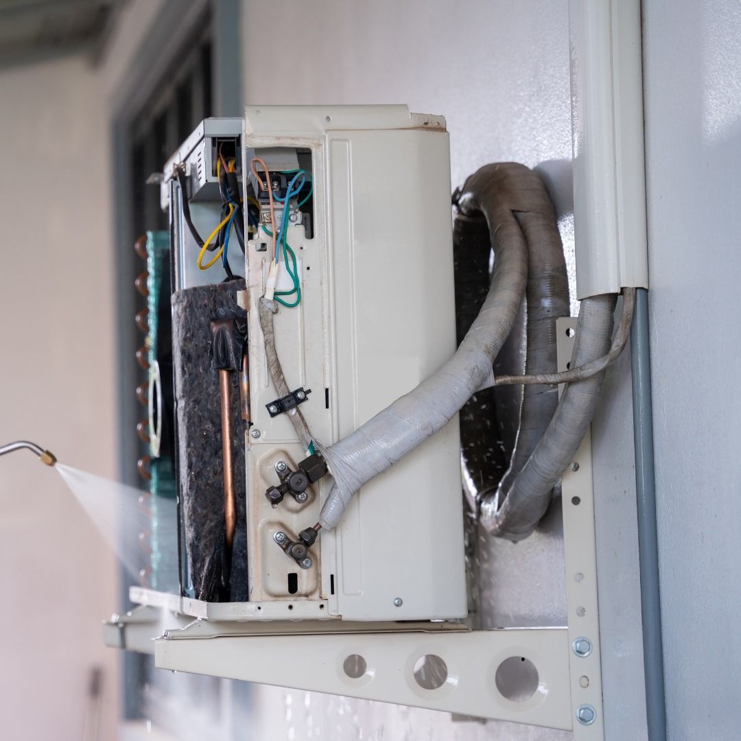 Una persona está rociando agua sobre un acondicionador de aire montado en la pared.