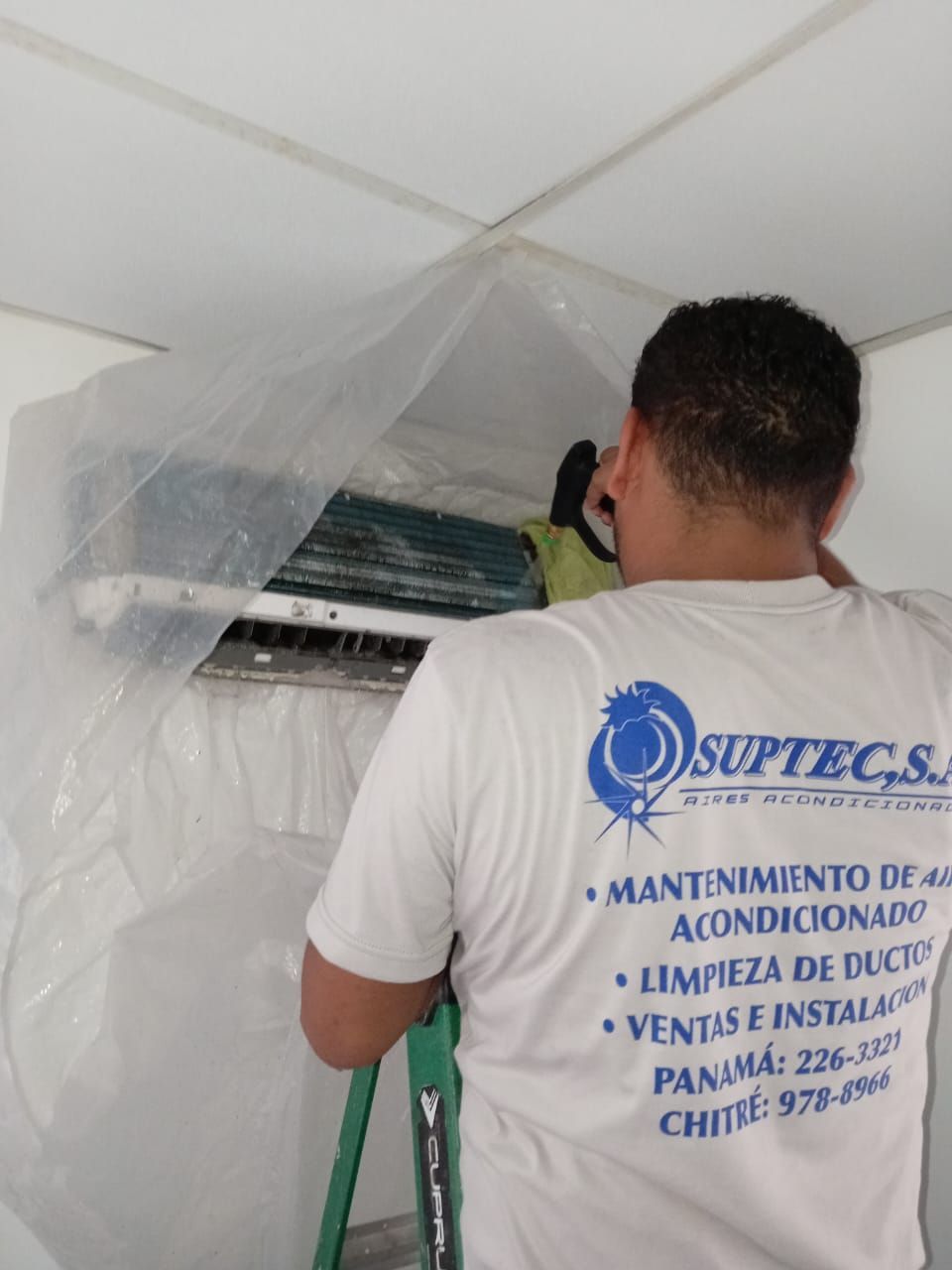 Un hombre que lleva una camiseta que dice Suptecs está trabajando en un aire acondicionado.