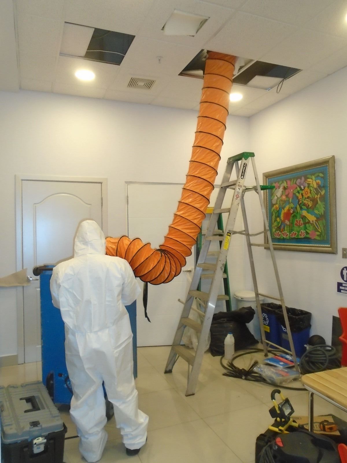 Un hombre con un traje blanco está de pie junto a una manguera naranja que cuelga del techo.