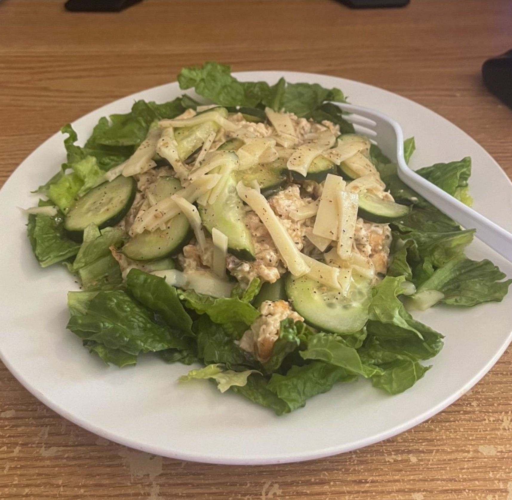 A white plate topped with a salad and a fork on a table.