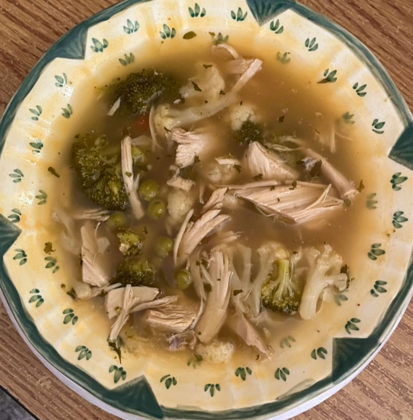 A bowl of soup with chicken broccoli and peas