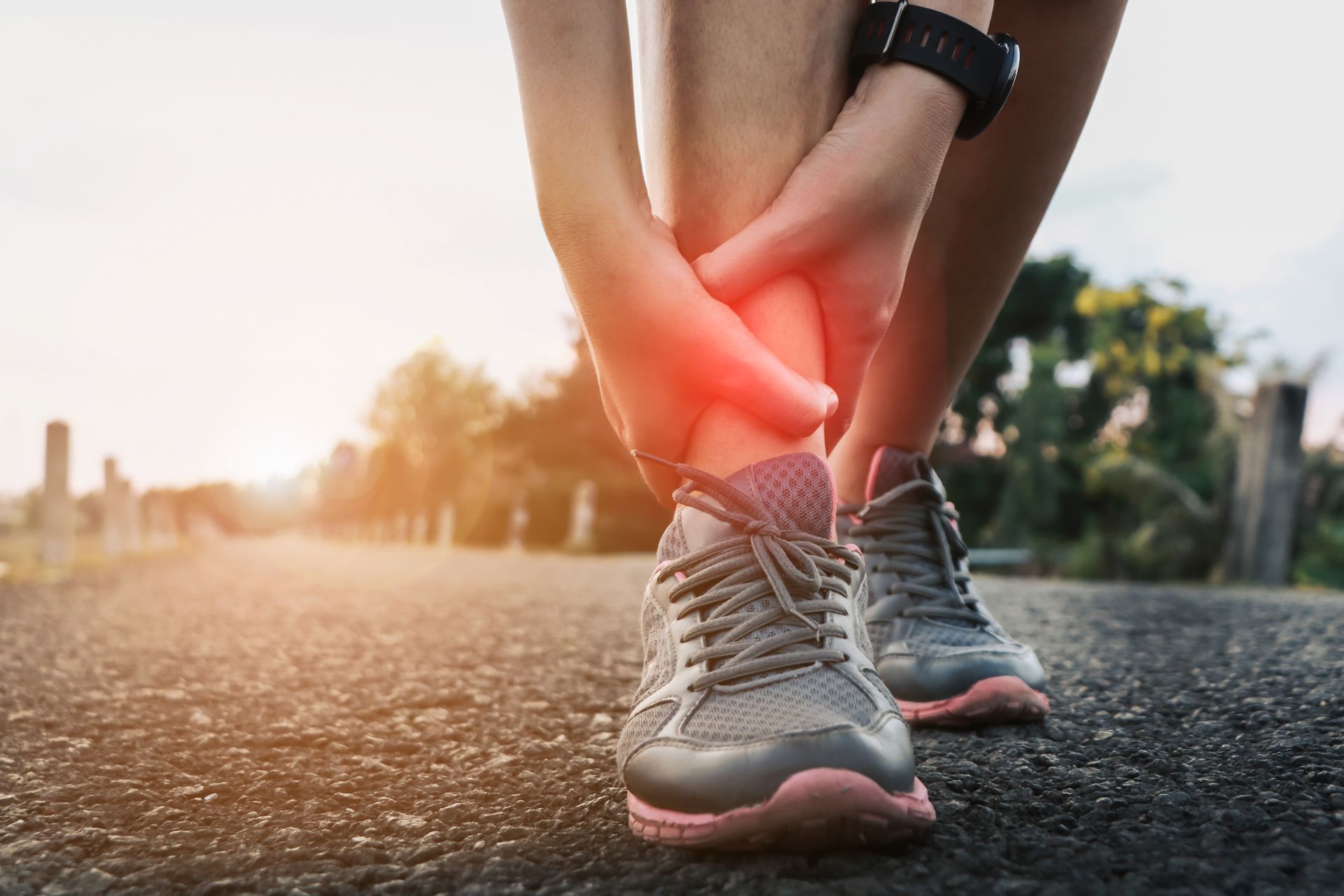 A person is holding their ankle in pain while running on a road