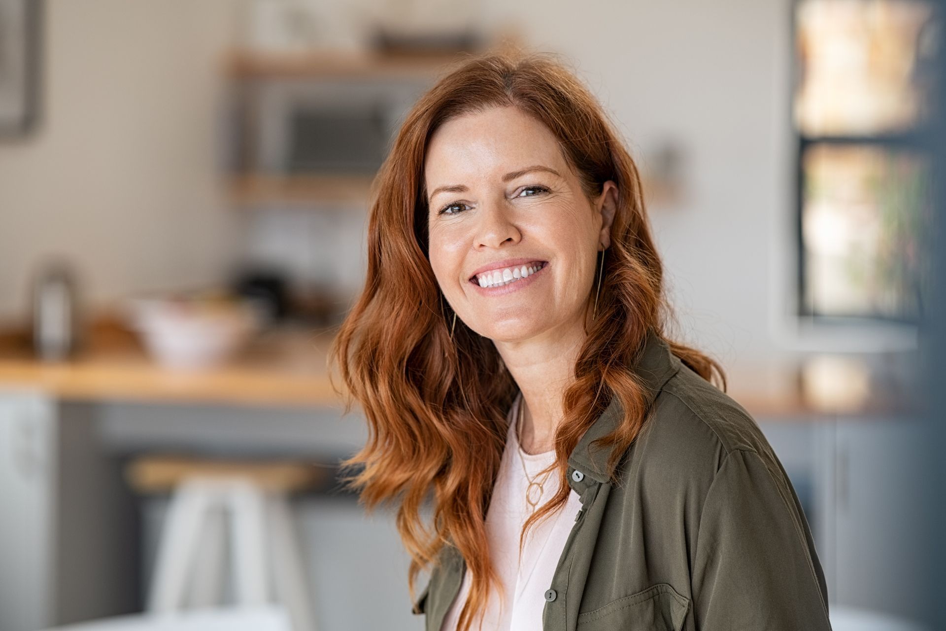 A woman with red hair is smiling for the camera in a kitchen