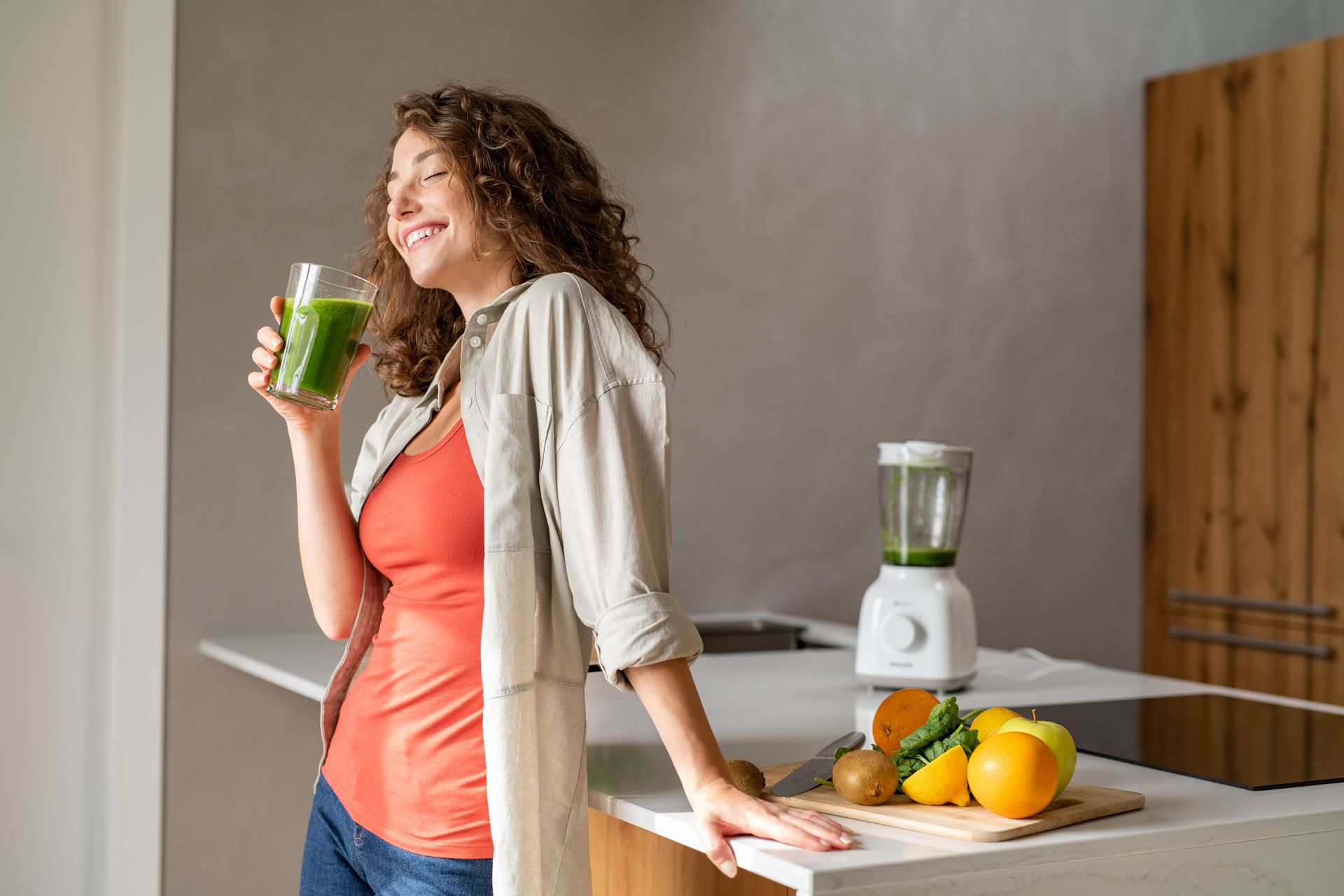 A pregnant woman is drinking a green smoothie in a kitchen