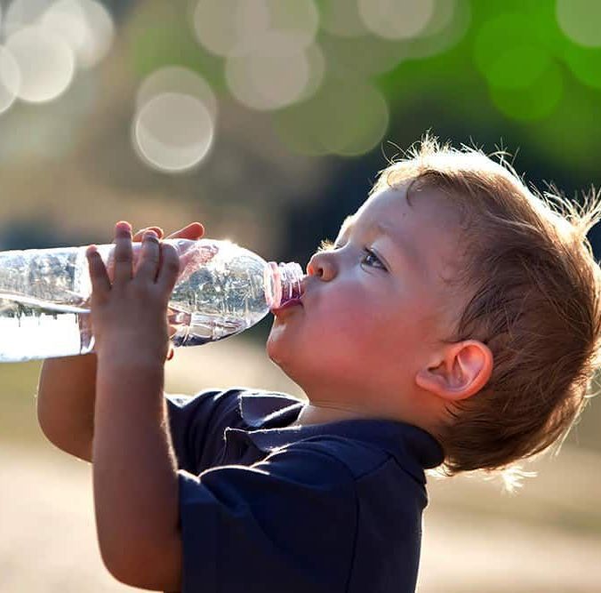 A young boy is drinking water from a plastic bottle