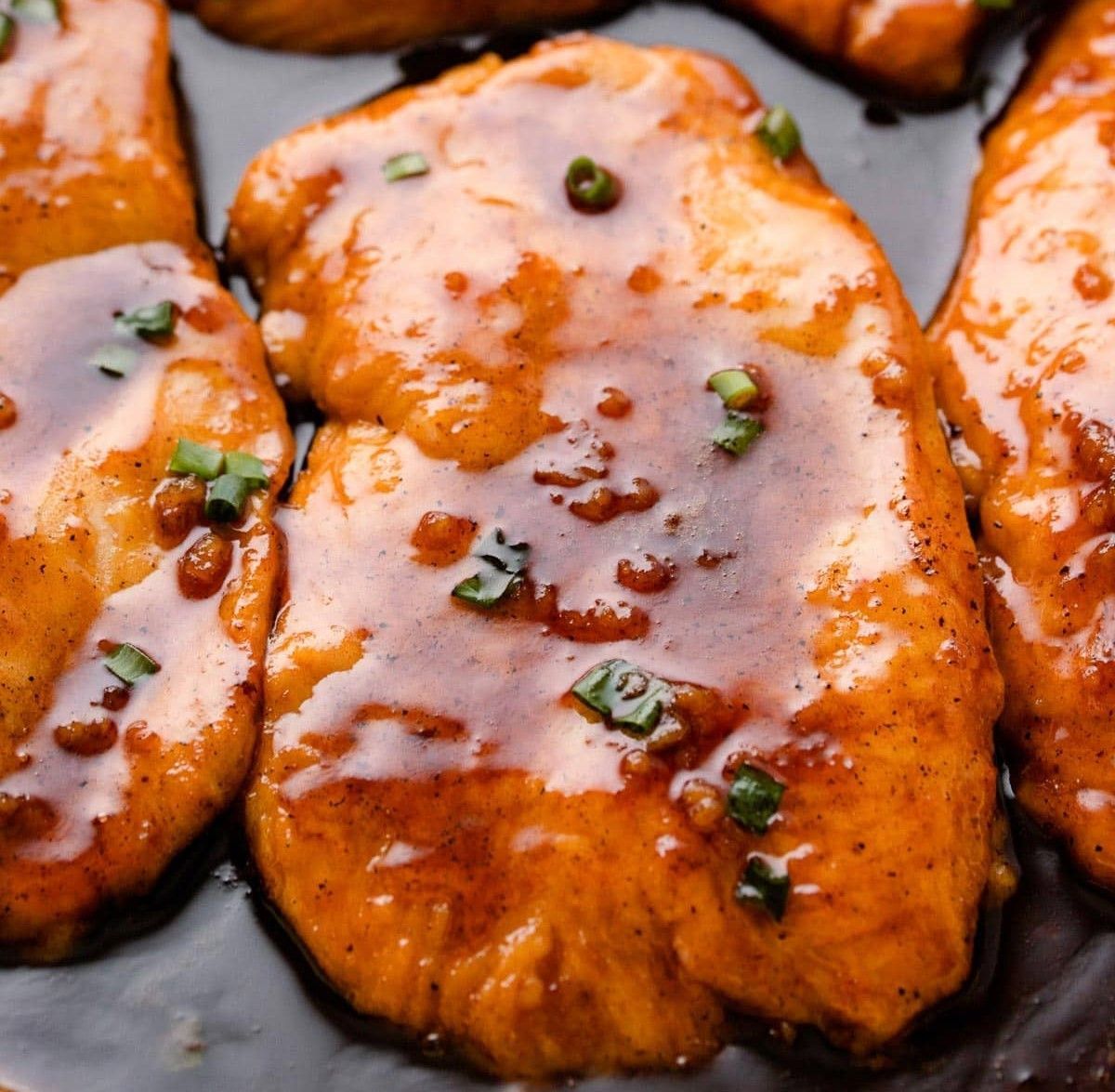 A close up of chicken covered in sauce and green onions