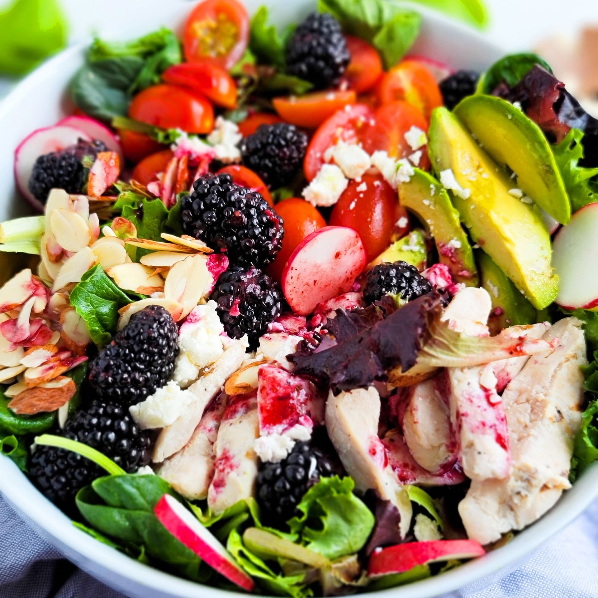 A salad with chicken , tomatoes , blackberries and almonds in a bowl