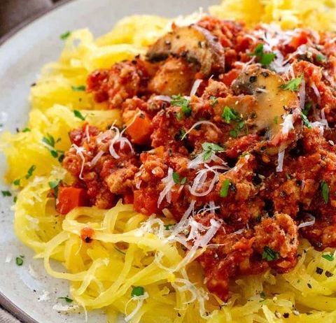 A close up of a plate of spaghetti squash with meat sauce and cheese.