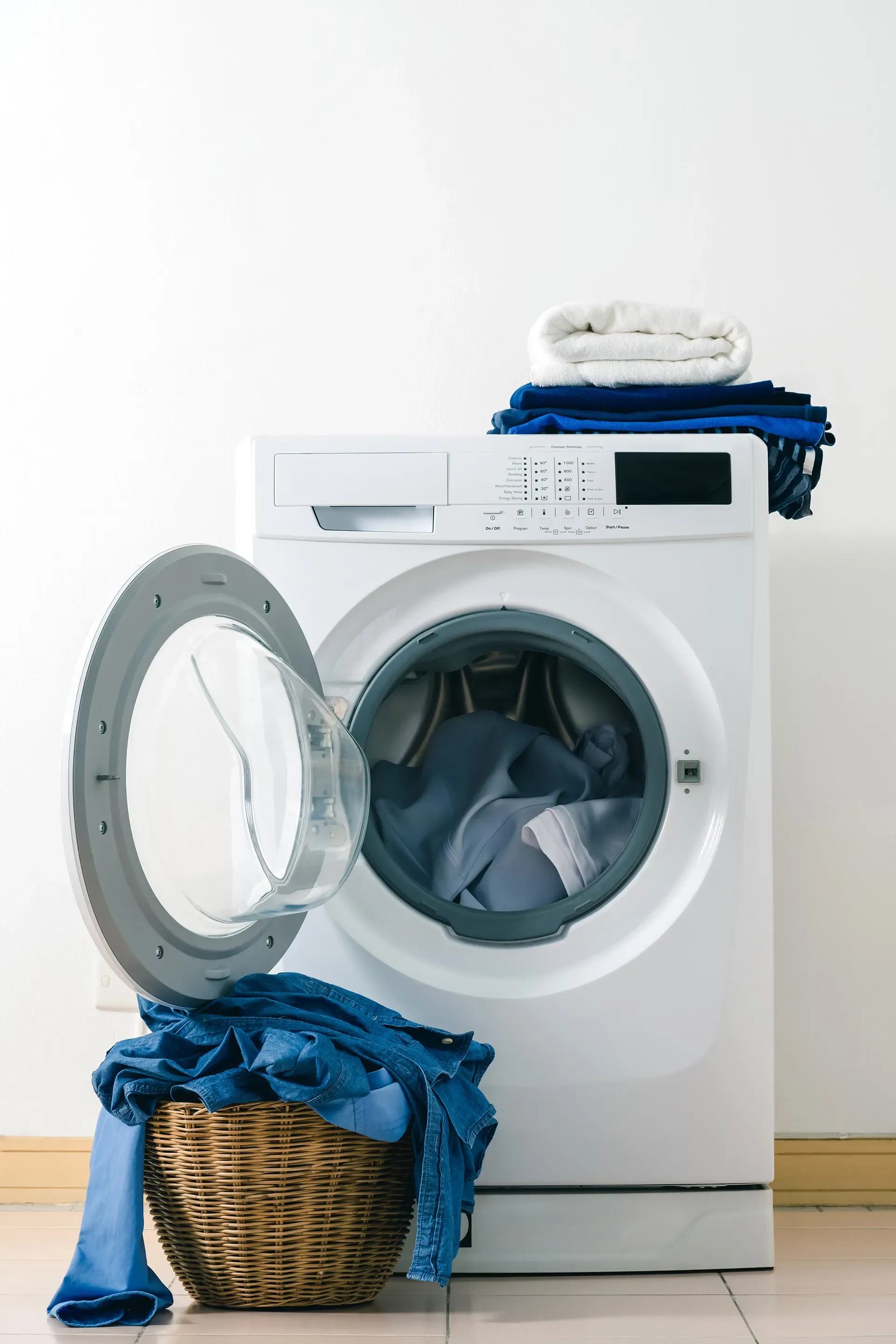 A washing machine with its door open and a basket of clothes next to it.