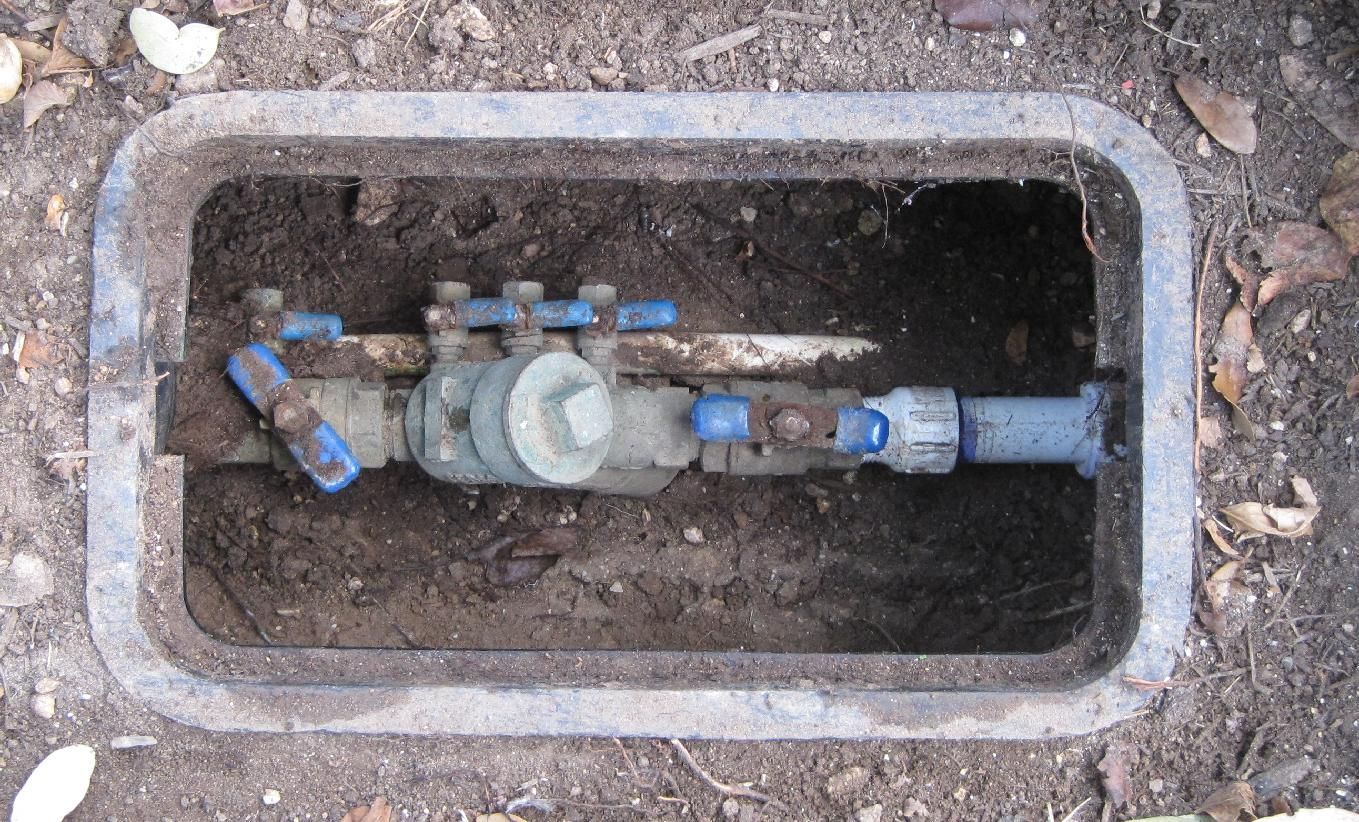A water meter is sitting in the dirt in a manhole cover