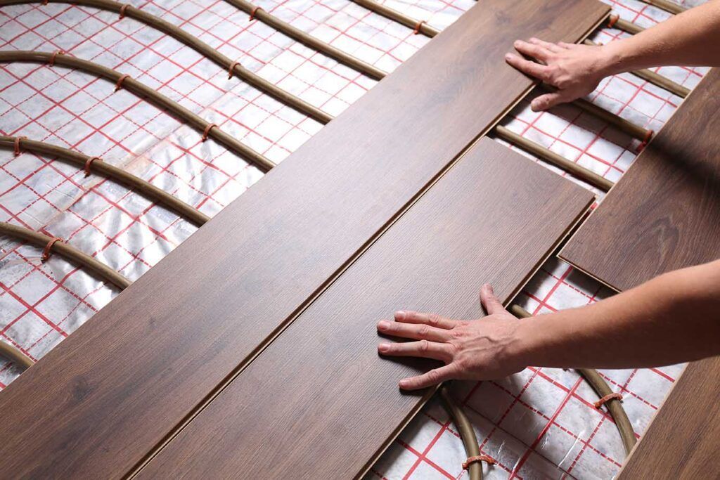 A person is installing a wooden floor with underfloor heating.