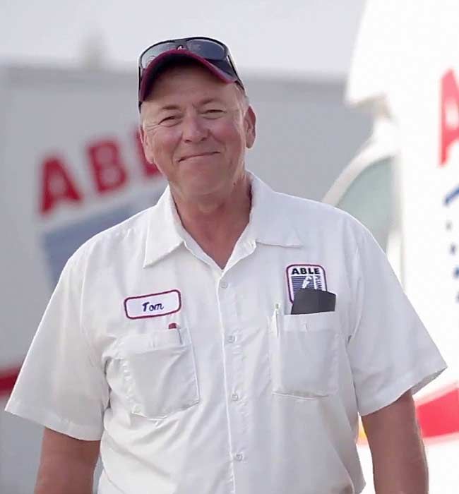 Smiling worker in white shirt and cap standing outdoors near aircraft, with ABB logo visible