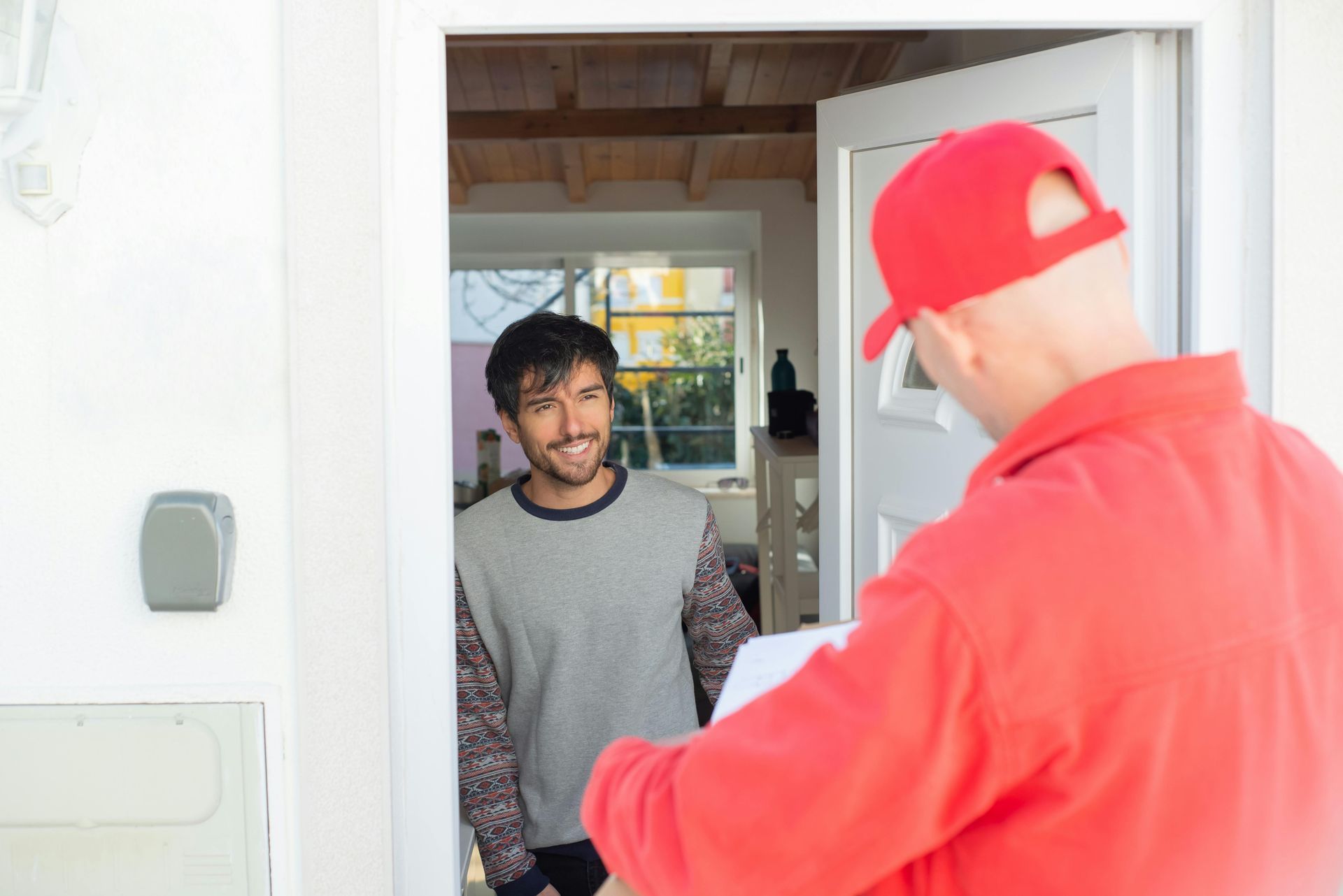 A delivery man is giving a package to a man in a doorway.