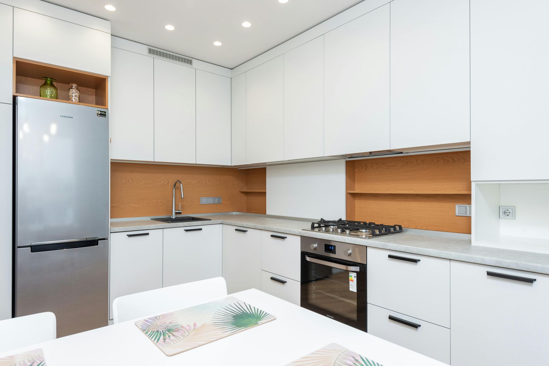 A kitchen with white cabinets , stainless steel appliances , a refrigerator , stove , oven and table.