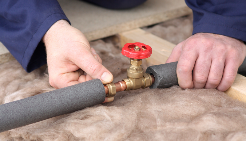 A man is fixing a pipe with a red valve.