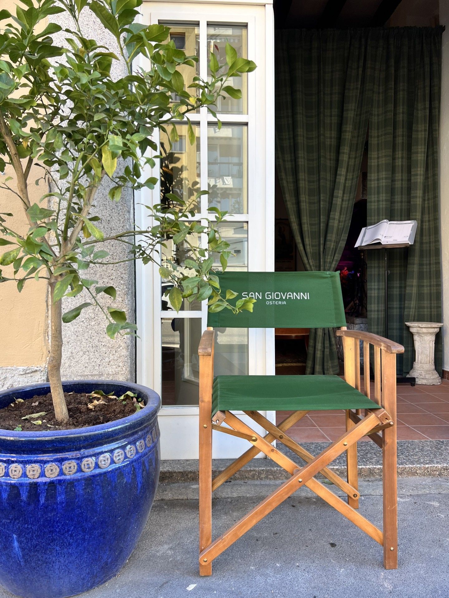 Una sedia da regista in tela verde è posizionata davanti a una porta, accanto a un albero in vaso.