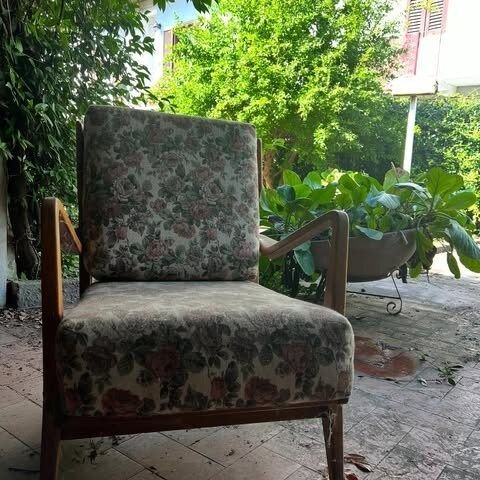 Una vecchia poltrona con motivi floreali è posizionata all'esterno.