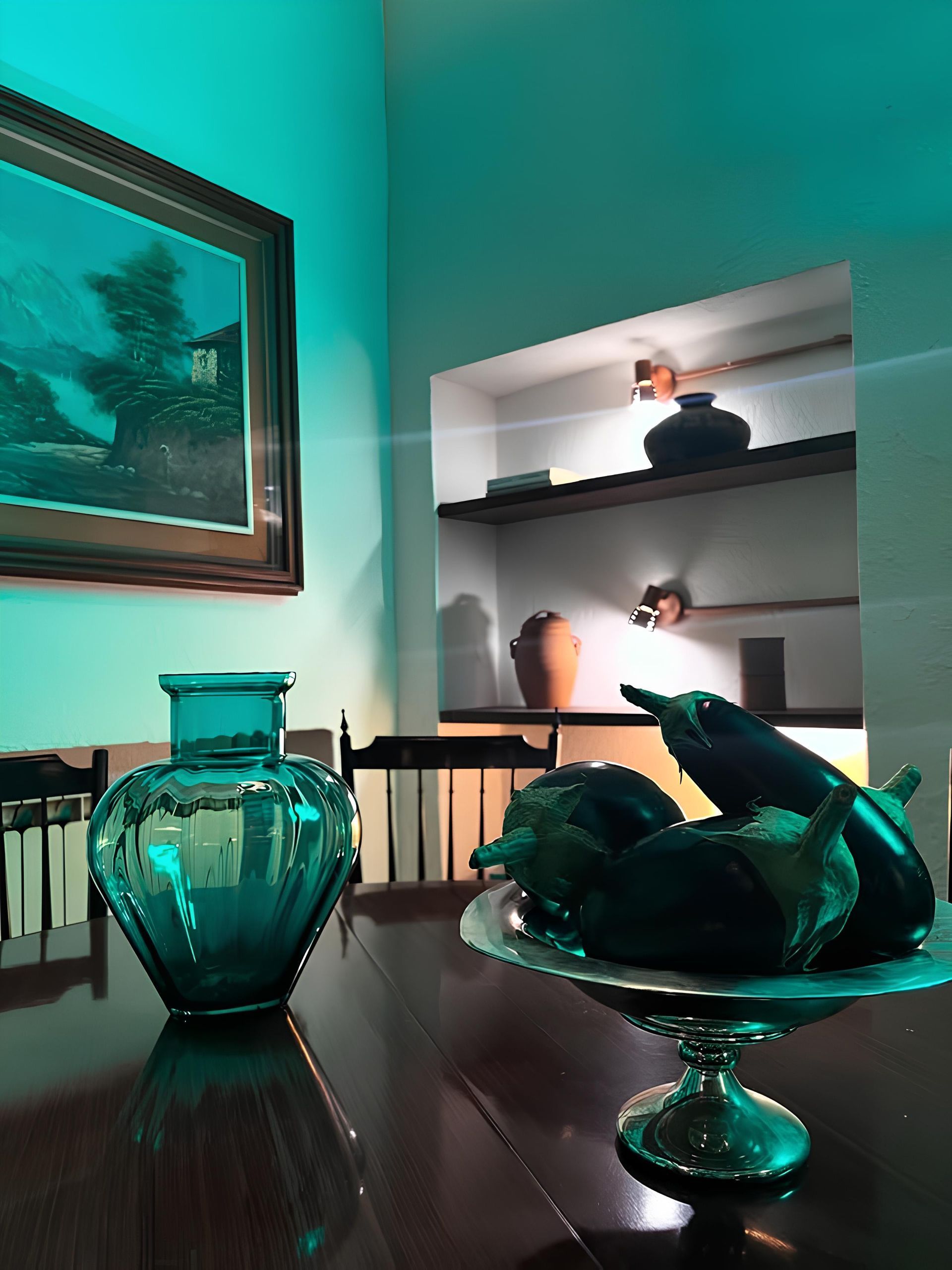 Vaso color verde acqua e melanzane in una ciotola d'argento su un tavolo scuro.