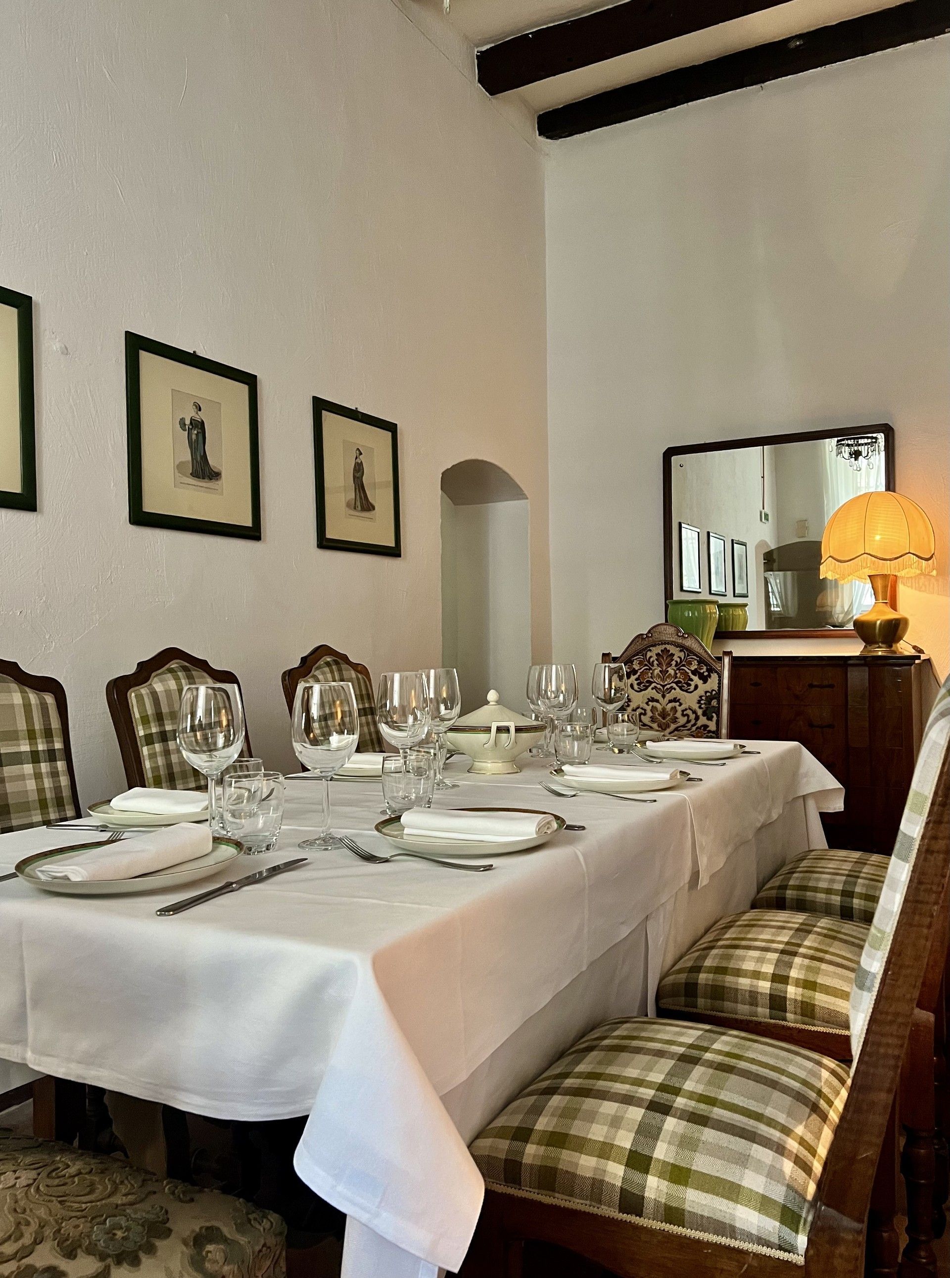 Sala da pranzo formale con lungo tavolo apparecchiato per un pasto. Sedie a quadri, tovaglia bianca e quadri incorniciati impreziosiscono lo spazio.