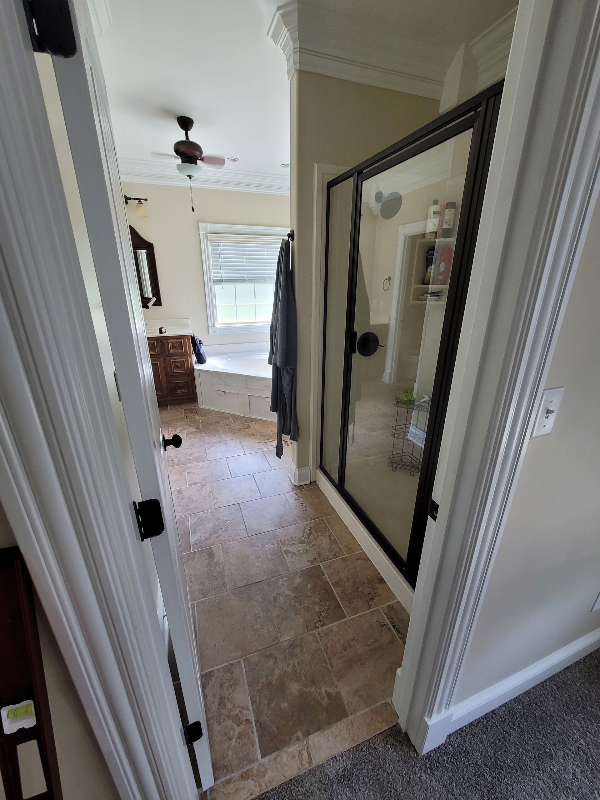 A view from a doorway into a bathroom with a tiled floor, a glass-enclosed shower, and a window with a built-in seat.