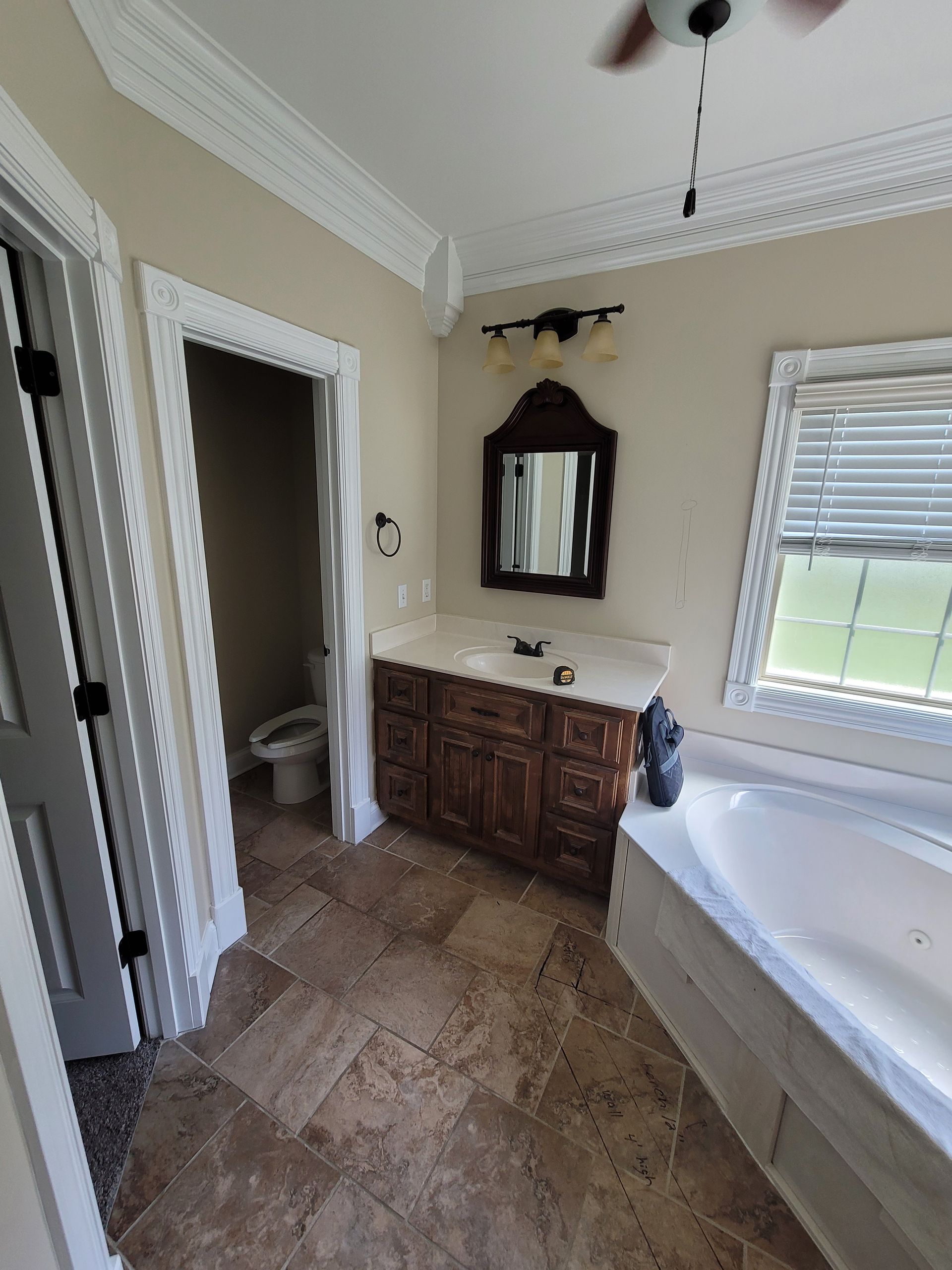 Bathroom featuring a dark wood vanity, stone-tiled floor, a wall-mounted mirror, a jetted tub, and an adjacent toilet closet.