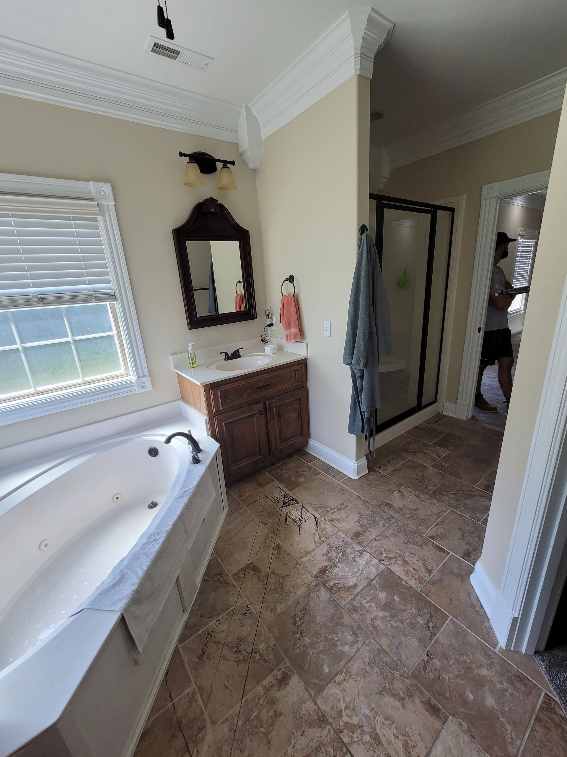 Bathroom with a white soaking tub, dark wood vanity, a mirror, and travertine tile flooring; a doorway leads to a shower.