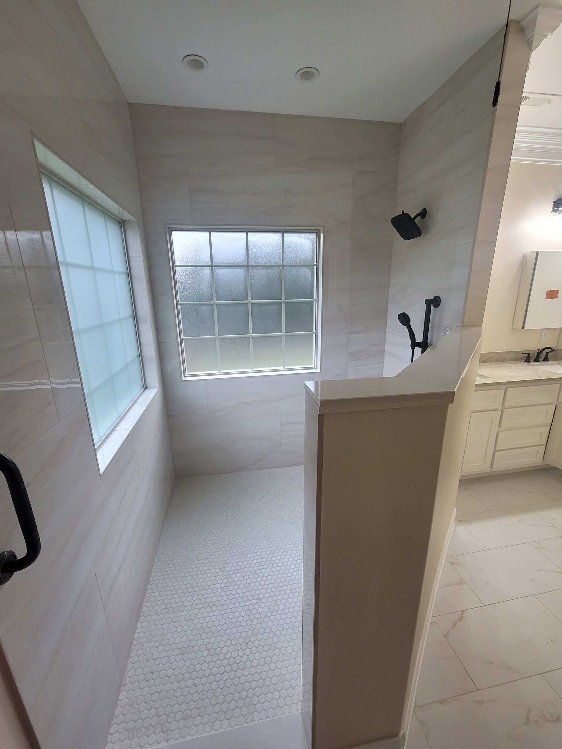 A modern walk-in shower with light beige tiled walls, a glass-block window, and a separate handheld showerhead fixture.