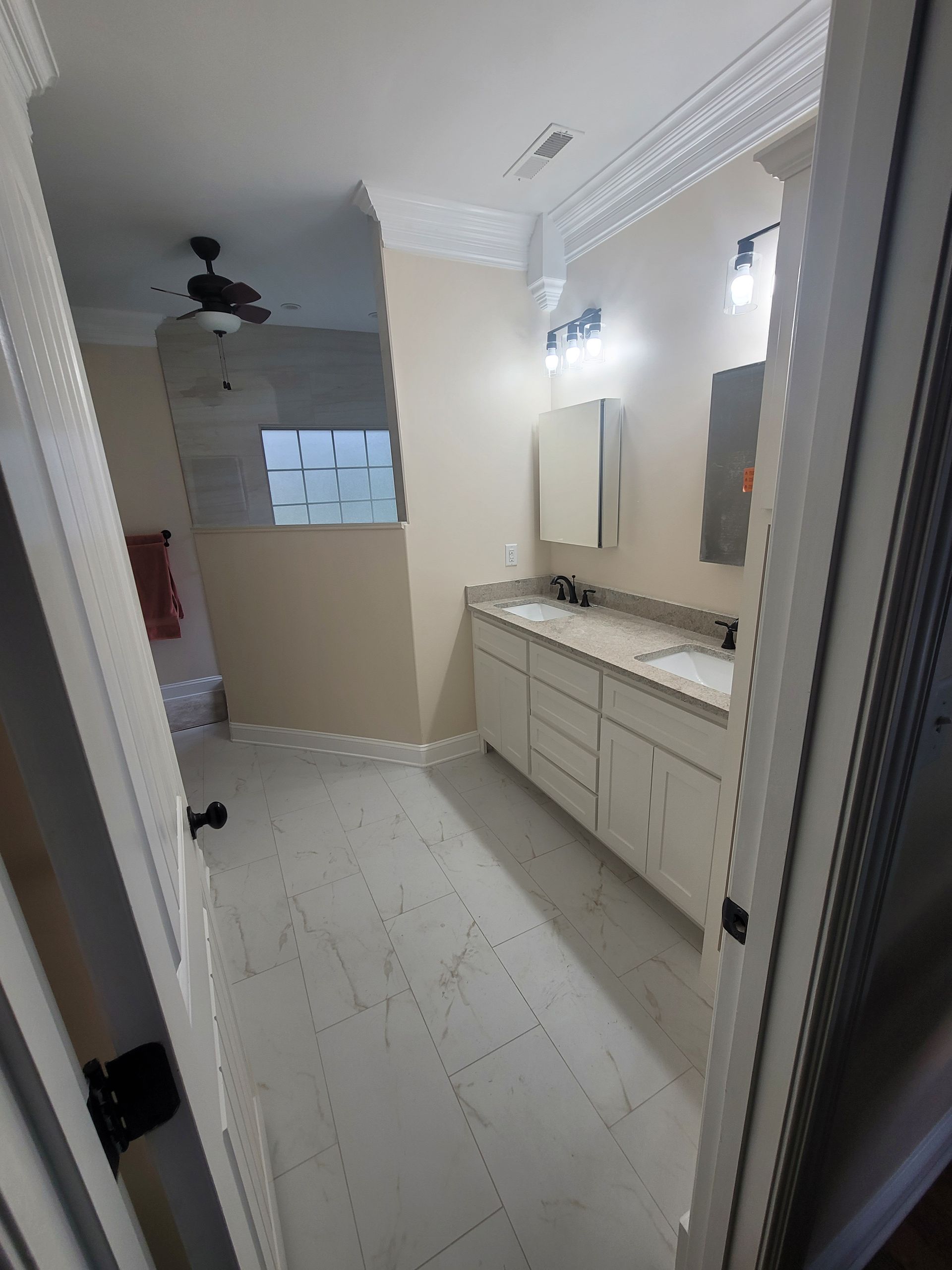 A modern bathroom features a double vanity with white cabinets, light-colored tile floors, and a walk-in shower area.