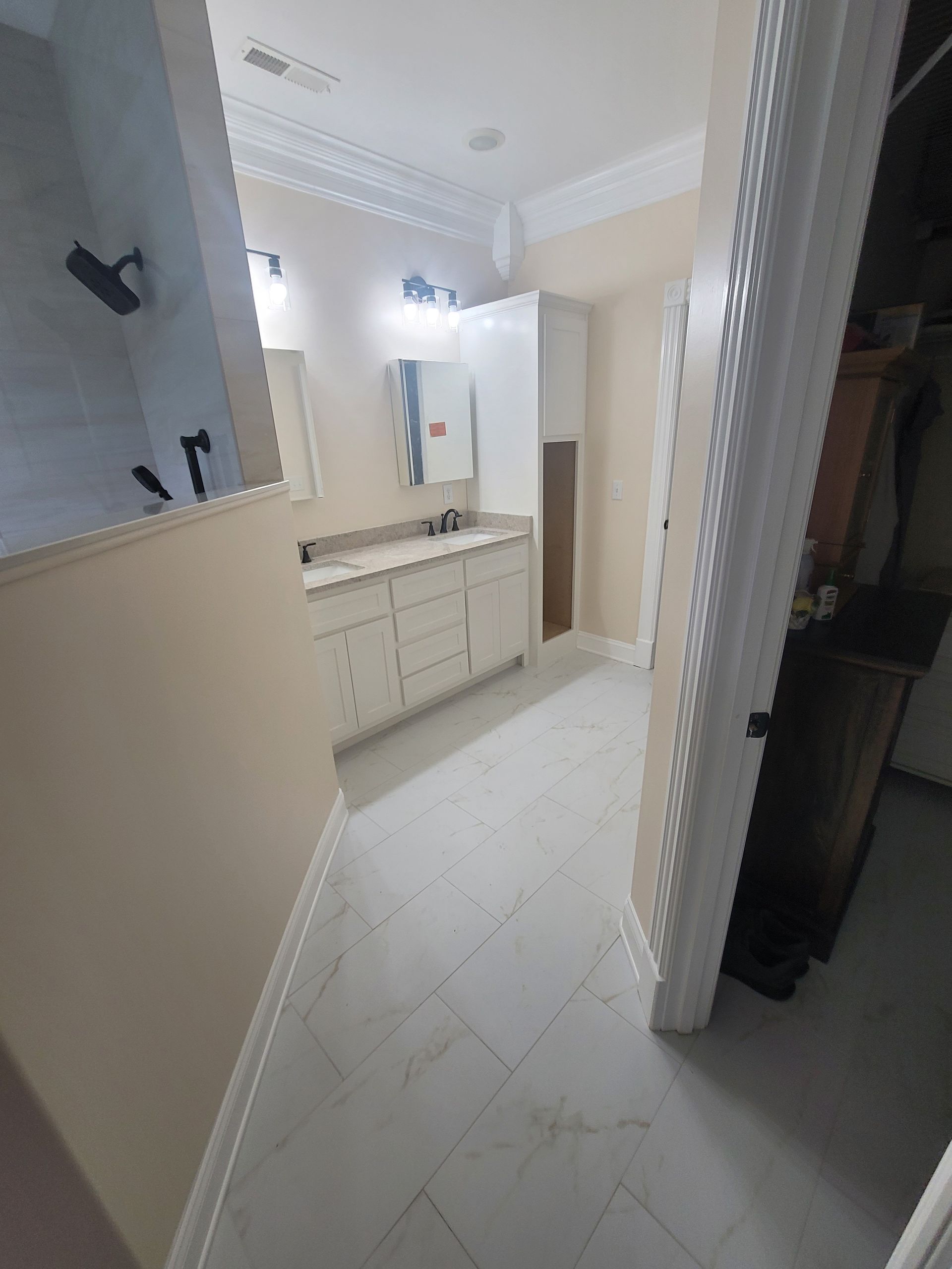A modern bathroom with white cabinets, a light-colored countertop, and light tile flooring, viewed from a doorway.