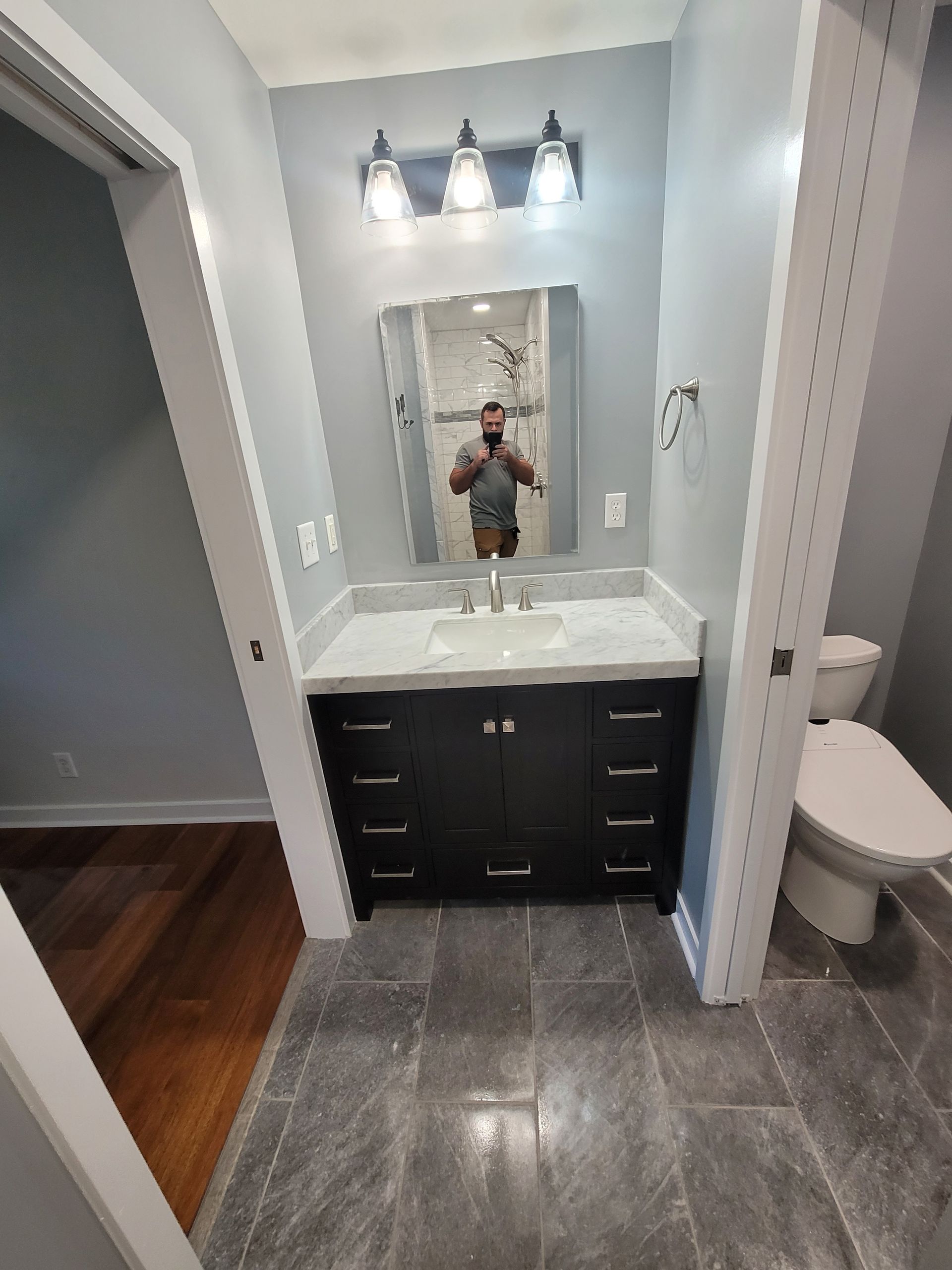 A bathroom vanity with a dark wood cabinet, marble countertop, mirror, and light fixture, next to a toilet.