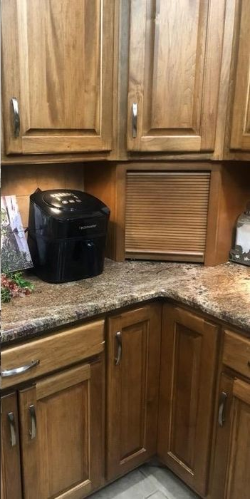 Black air fryer on a granite countertop in a kitchen with wooden cabinets and a tambour door appliance garage.