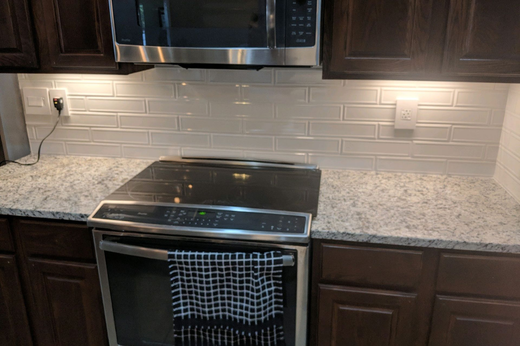 A kitchen scene featuring a dark wood stove, granite countertops, a white subway tile backsplash, and a microwave.
