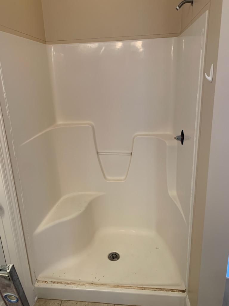 A cream-colored, walk-in shower stall with an integrated corner seat, soap dish, and overhead showerhead.