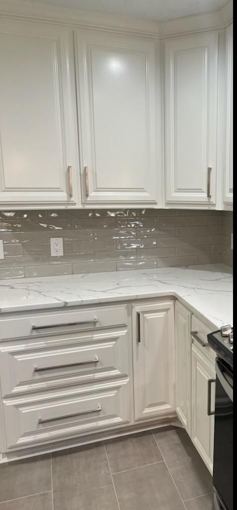 A kitchen featuring white cabinets, a light stone countertop, and a glossy, horizontal tile backsplash in a neutral tone.