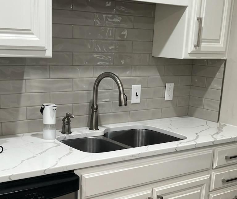 A kitchen sink with a chrome faucet, white veined marble countertops, and light gray rectangular tile backsplash.