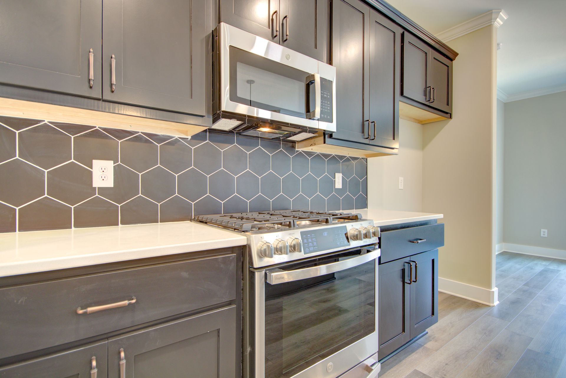 A modern kitchen with dark grey cabinets, a white countertop, a stainless steel stove, and a grey hexagon tile backsplash.