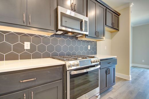 A modern kitchen with dark grey cabinets, a white countertop, a stainless steel stove, and a grey hexagon tile backsplash.